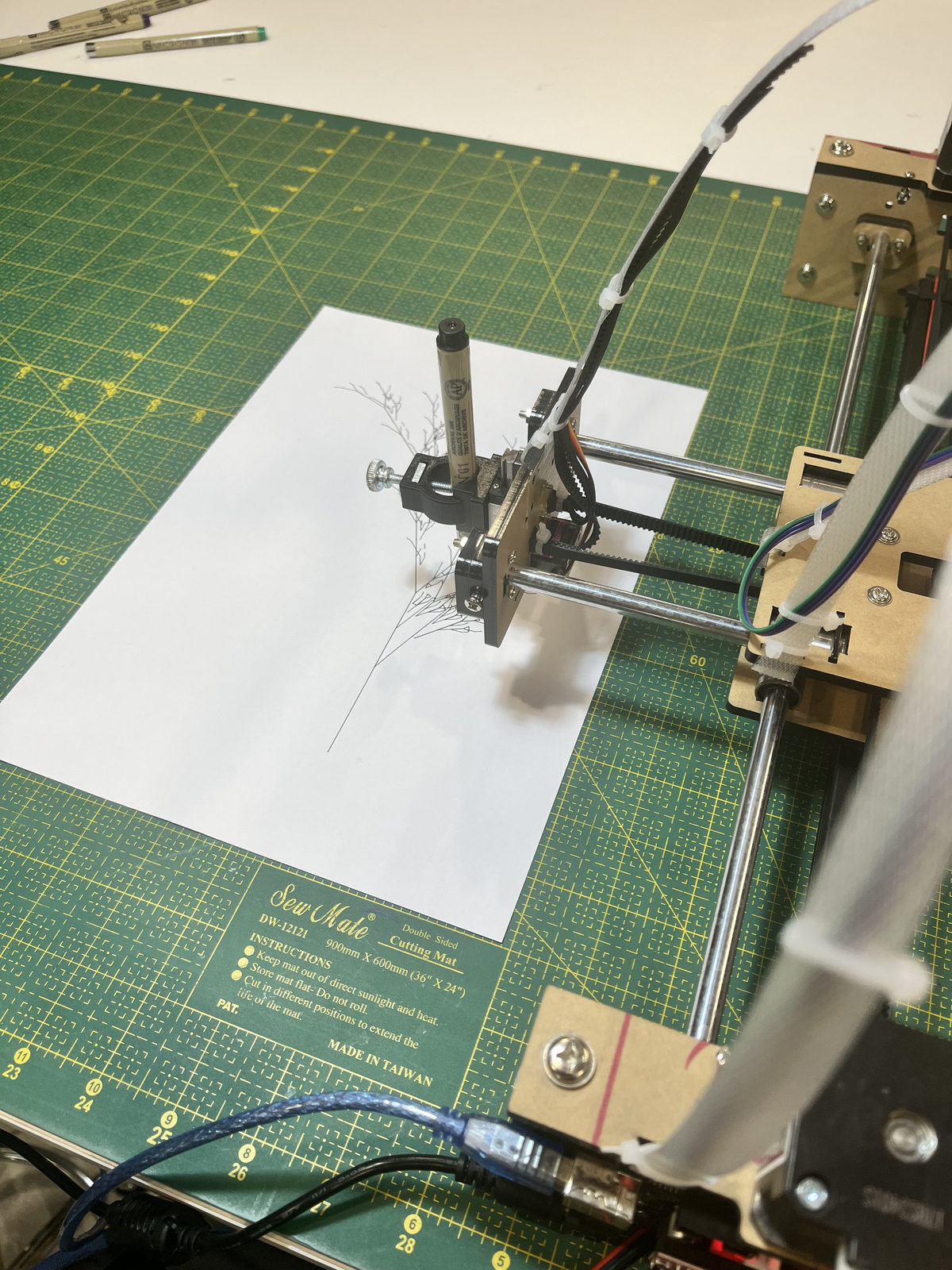 Overhead view of Drawdroid drawing a botanical line artwork with a real pen