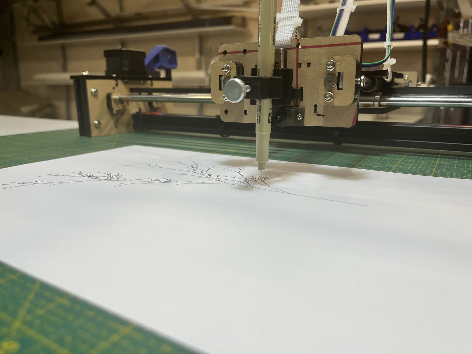 Drawdroid pen plotter mid-draw, making an ink botanical line drawing on paper