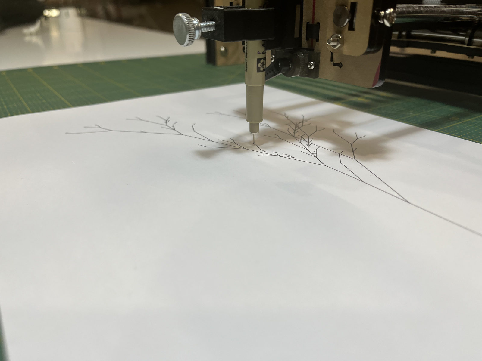 Close-up of a Drawdroid plotter pen drawing fine ink branches on archival paper