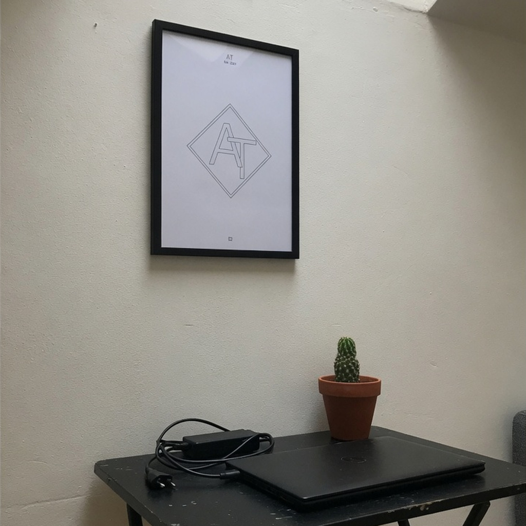 AT 2021 diamond monogram in a thin black frame above a folding desk in a rented studio